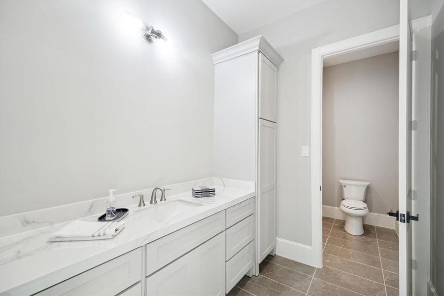This is a modern, clean bathroom featuring a large vanity with ample storage and marble countertop, a separate toilet area for privacy, and tiled flooring.