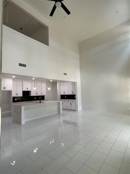 Unfurnished living room with sink, light tile patterned flooring, ceiling fan, and a towering ceiling