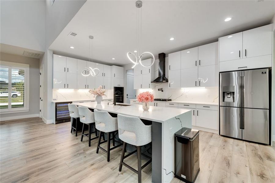 Kitchen with pendant lighting, light hardwood / wood-style flooring, stainless steel fridge with ice dispenser, and white cabinetry