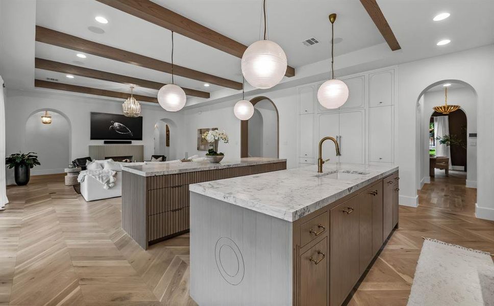 Kitchen featuring light parquet floors, light stone countertops, sink, pendant lighting, and a center island with sink