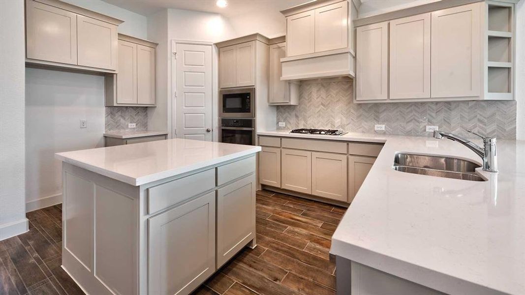 Kitchen with black microwave, sink, decorative backsplash, stainless steel oven, and a center island