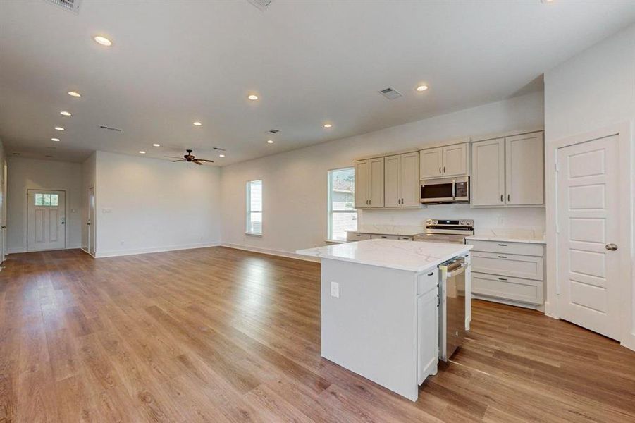 Kitchen featuring a kitchen island, light hardwood / wood-style flooring, appliances with stainless steel finishes, light stone counters, and ceiling fan