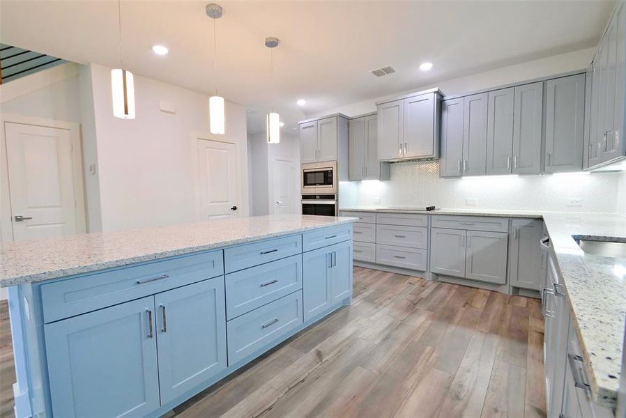 Kitchen with hanging light fixtures, decorative backsplash, stainless steel appliances, light wood-type flooring, and a center island