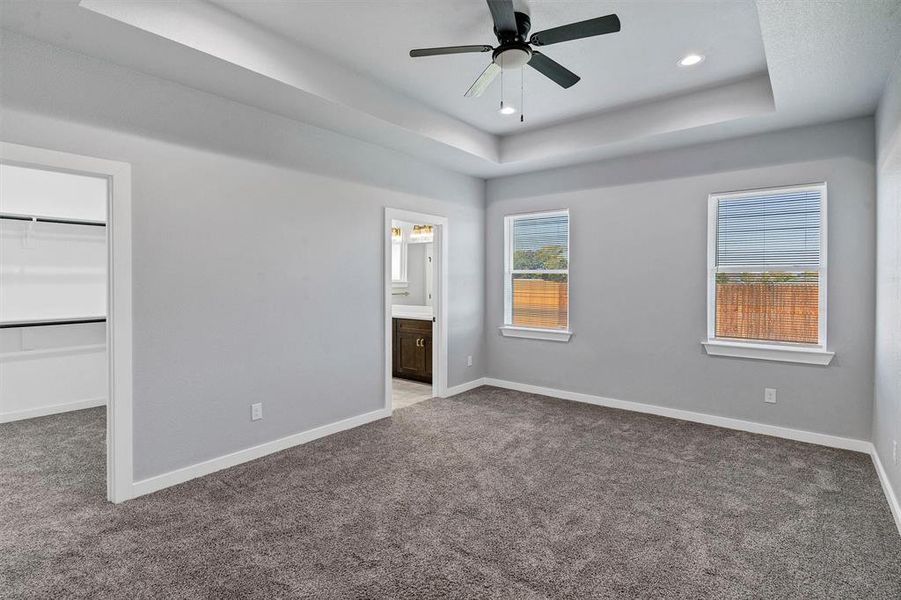 Unfurnished bedroom with a closet, a raised ceiling, ensuite bathroom, a spacious closet, and ceiling fan