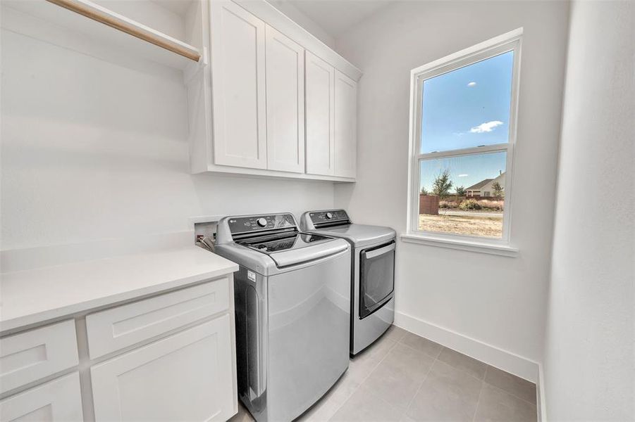 Laundry room featuring separate washer and dryer, light tile patterned floors, and cabinets