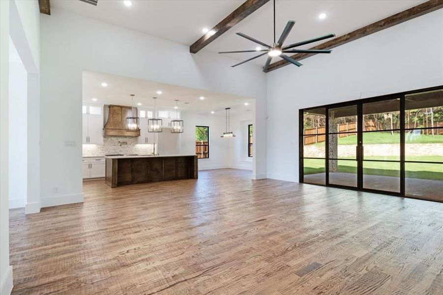 Unfurnished living room with beamed ceiling, a towering ceiling, light wood-type flooring, and ceiling fan