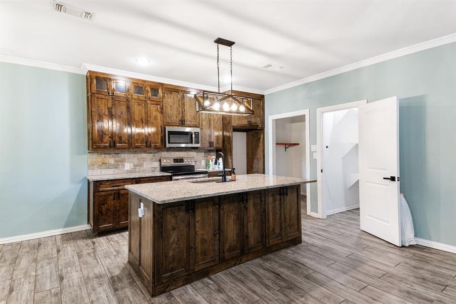 Kitchen with stainless steel appliances, light hardwood / wood-style floors, hanging light fixtures, and a center island with sink