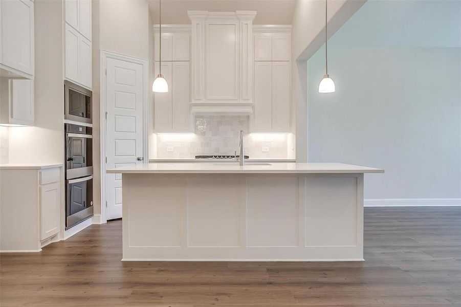 Kitchen featuring white cabinets, decorative backsplash, stainless steel microwave, and wood-type flooring