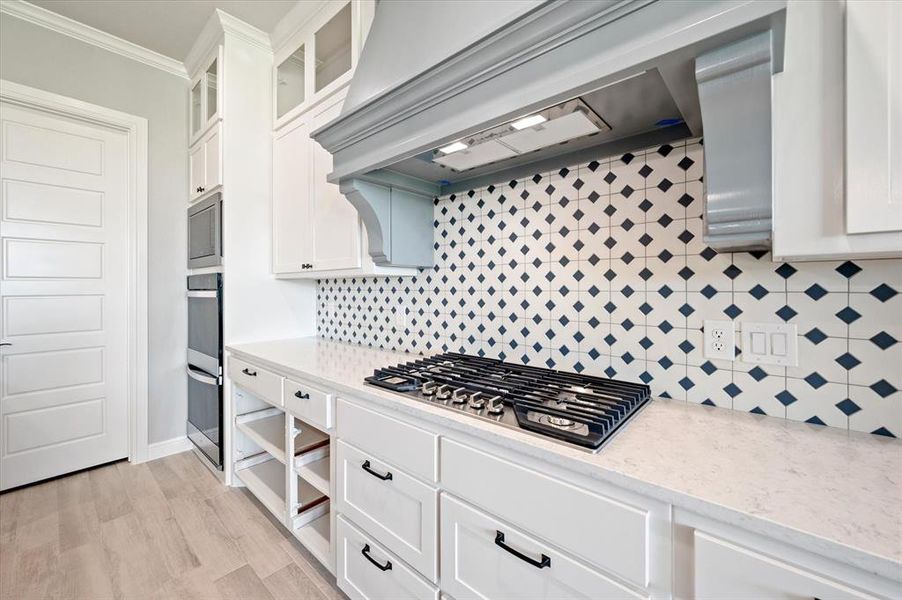 Kitchen with appliances with stainless steel finishes, white cabinets, backsplash, light wood-type flooring, and ornamental molding