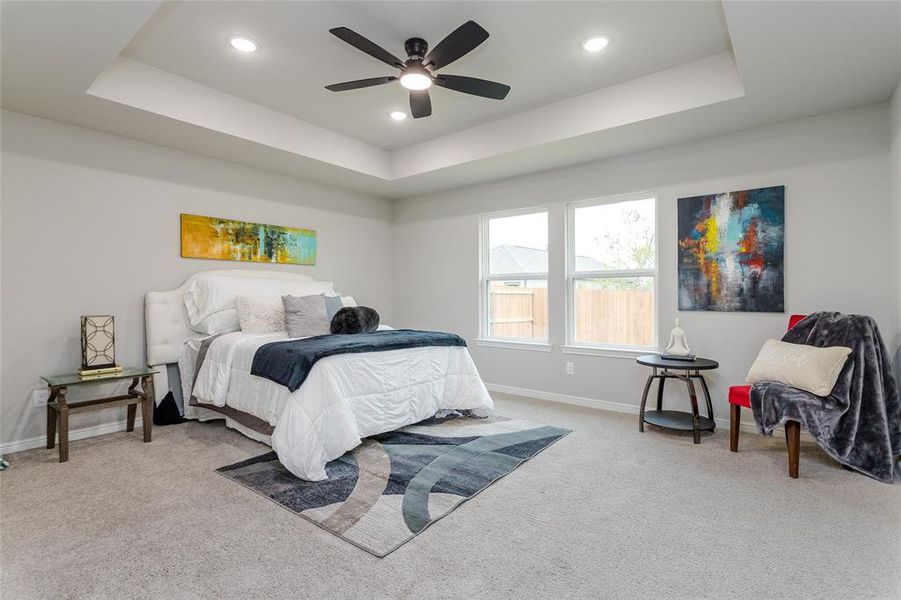 Bedroom with light carpet, a tray ceiling, and ceiling fan