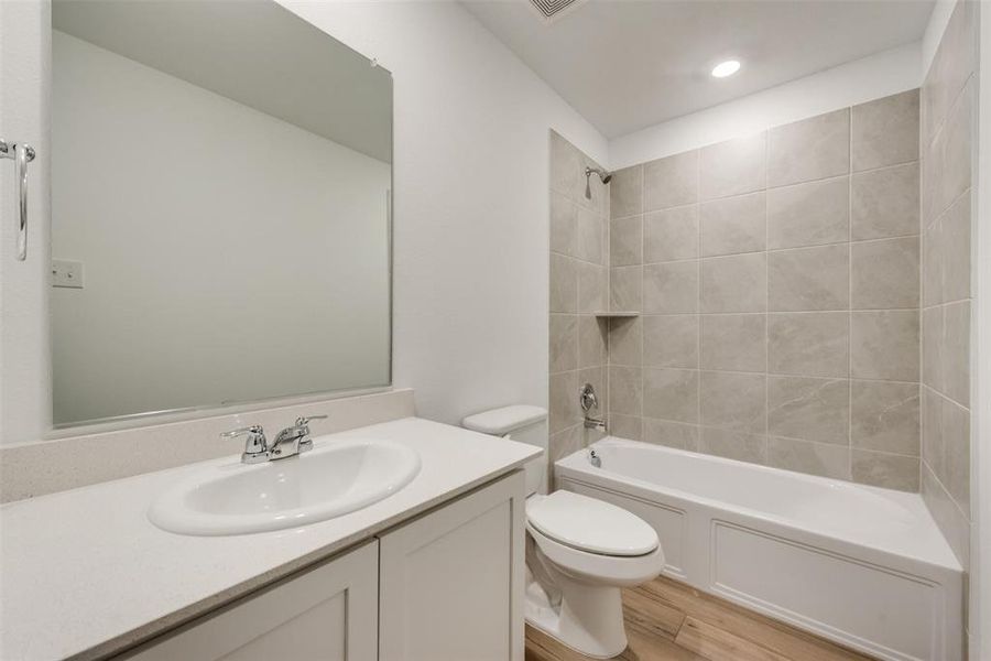 Full bathroom with vanity, toilet, tiled shower / bath combo, and hardwood / wood-style flooring