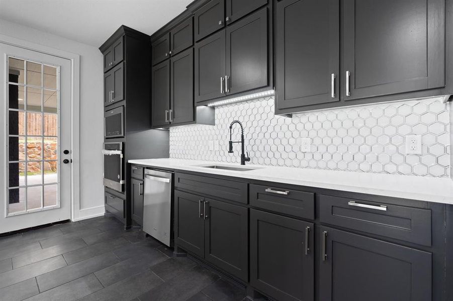 Kitchen with appliances with stainless steel finishes, decorative backsplash, sink, and dark tile patterned floors