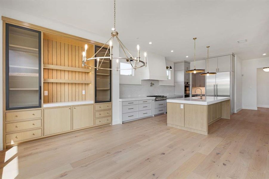 Kitchen with a large island with sink, light hardwood / wood-style flooring, decorative backsplash, an inviting chandelier, and decorative light fixtures