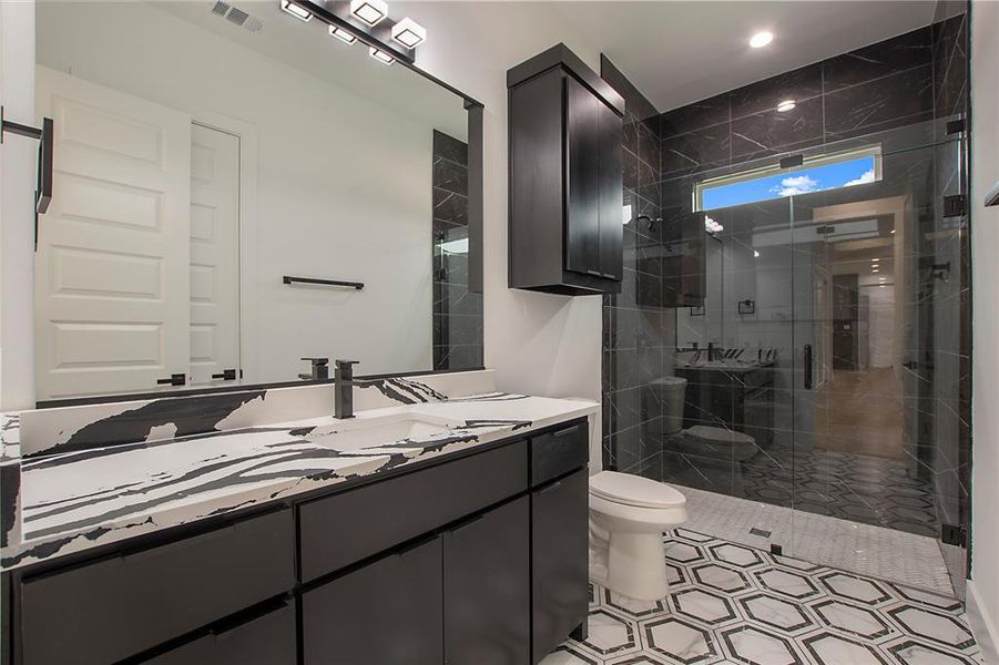 Bathroom featuring a shower with shower door, vanity, tile patterned floors, and toilet