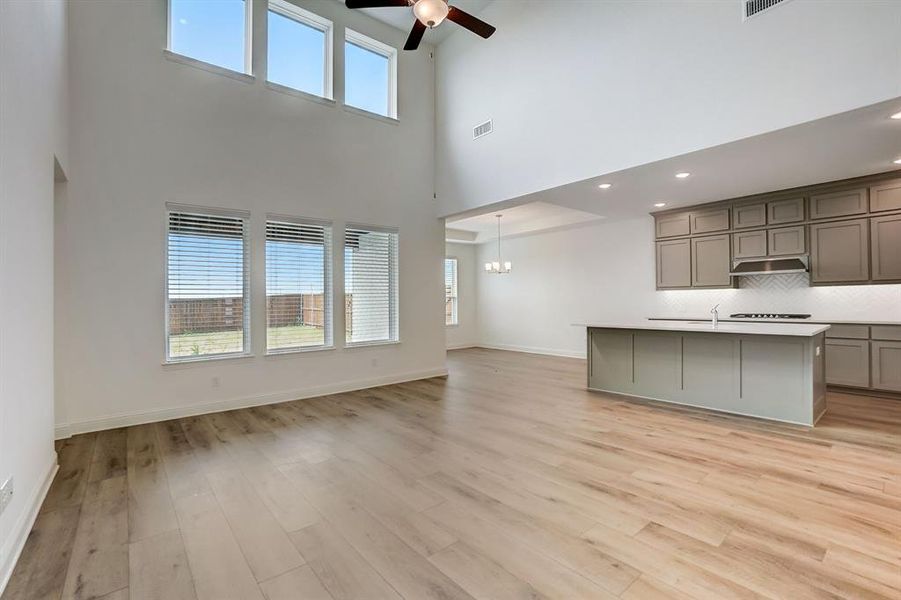 Kitchen featuring plenty of natural light, light hardwood / wood-style floors, ceiling fan with notable chandelier, tasteful backsplash, and a kitchen island with sink