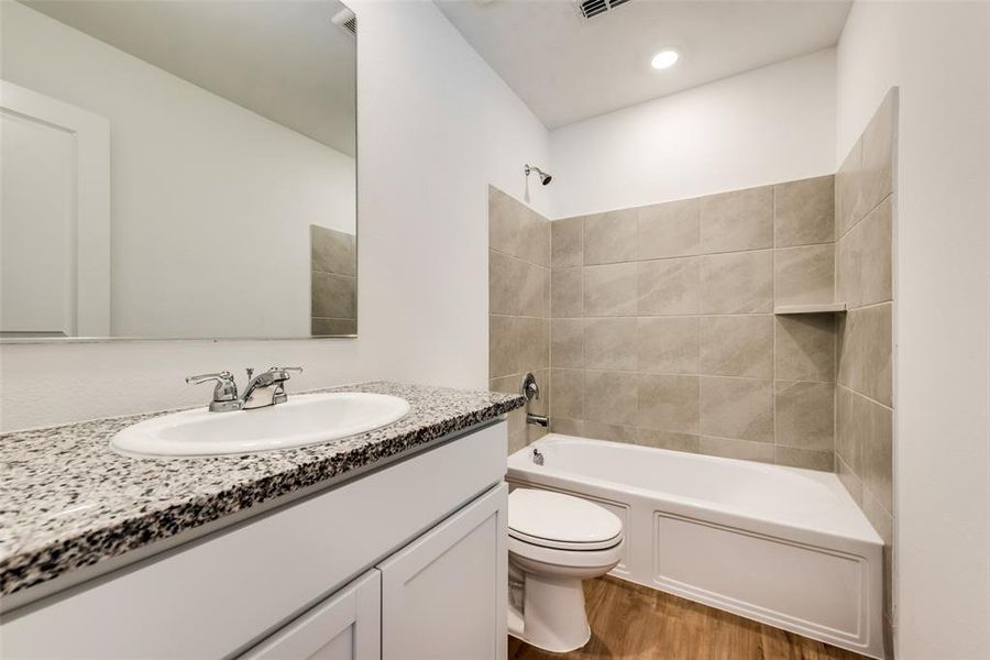 Full bathroom with vanity, toilet, tiled shower / bath, and hardwood / wood-style floors