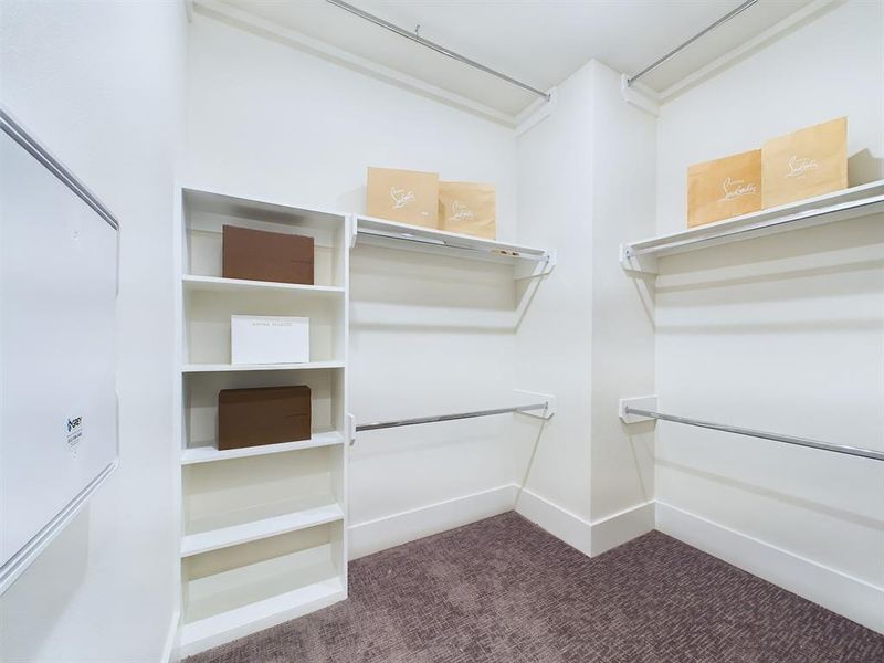 Create your own version of a luxury wardrobe area thanks to this closet inside the primary bathroom! Enjoy the convenience of additional hanging racks and built-in storage, providing ample space for your capsule and seasonal pieces. Wide baseboards and plush carpeting add a sparkle of elegance to this well-appointed & organized space! *All interior photos are from the model home: 2915 Paul Quinn.*