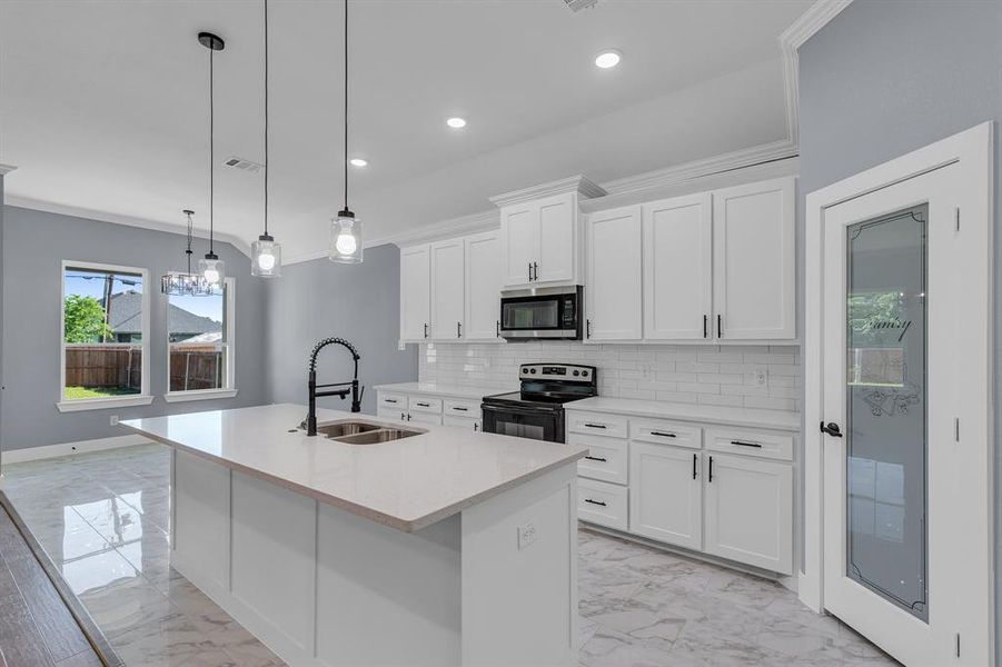 Kitchen featuring appliances with stainless steel finishes, a kitchen island with sink, backsplash, pendant lighting, and sink