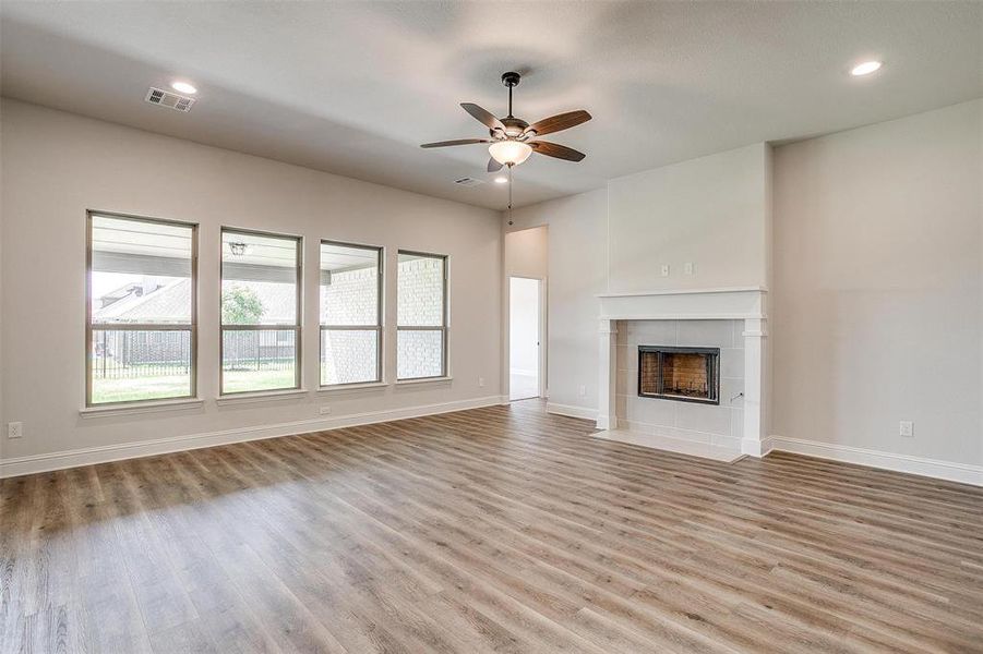 Unfurnished living room featuring a tile fireplace, ceiling fan, and light hardwood / wood-style floors