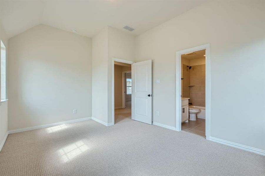 Unfurnished bedroom with light colored carpet, lofted ceiling, and ensuite bathroom