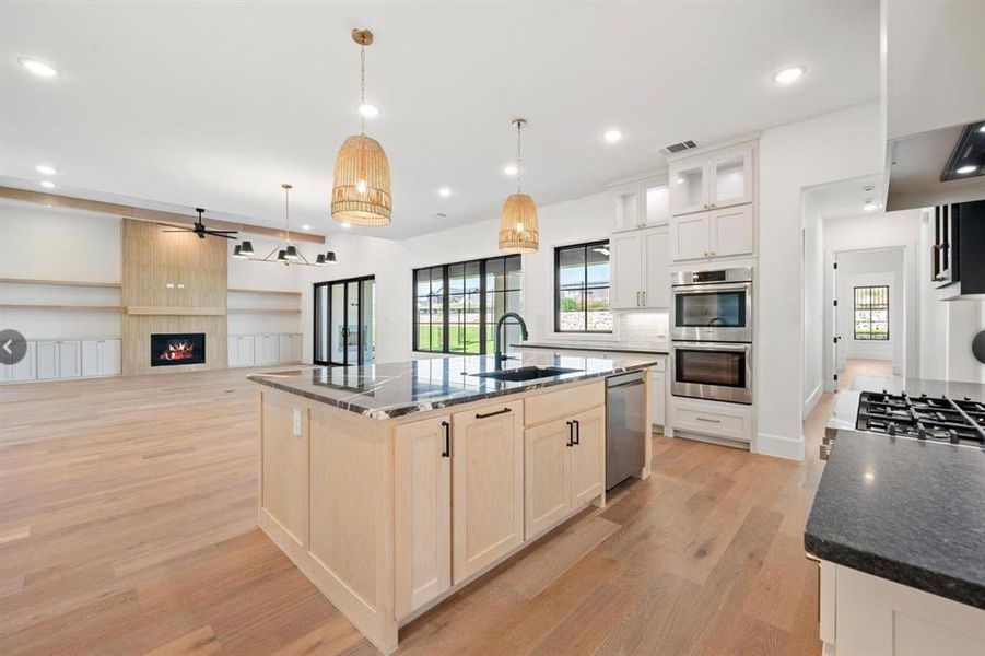 Kitchen featuring light wood-type flooring, a large fireplace, stainless steel appliances, sink, and a center island with sink