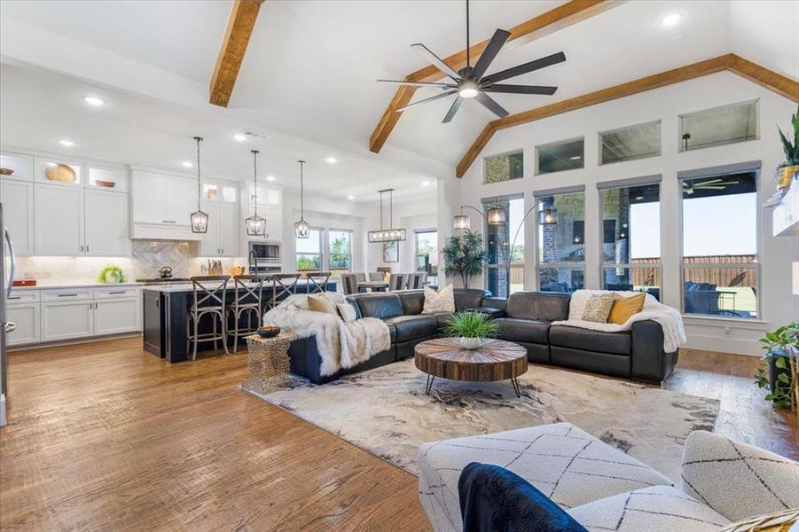 Living room with ceiling fan with notable chandelier, light wood-type flooring, beamed ceiling, and high vaulted ceiling