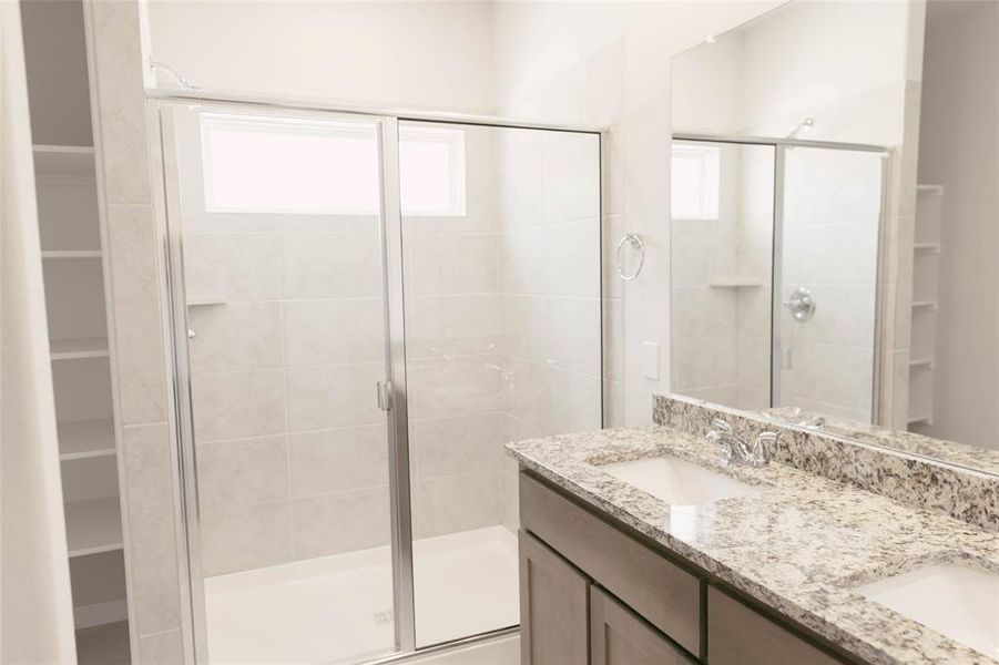 Bathroom featuring a shower with shower door, double sink vanity, and plenty of natural light