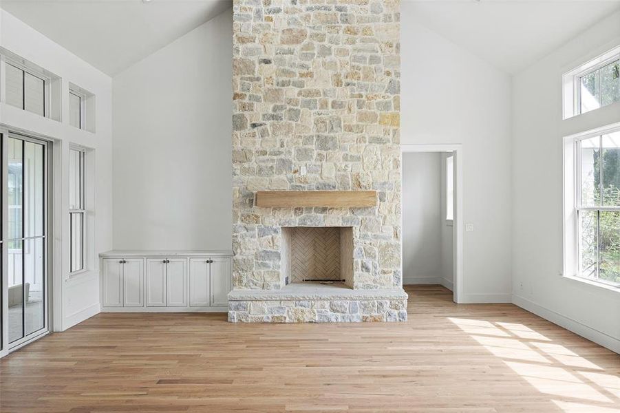 Unfurnished living room with high vaulted ceiling, a wealth of natural light, and a stone fireplace