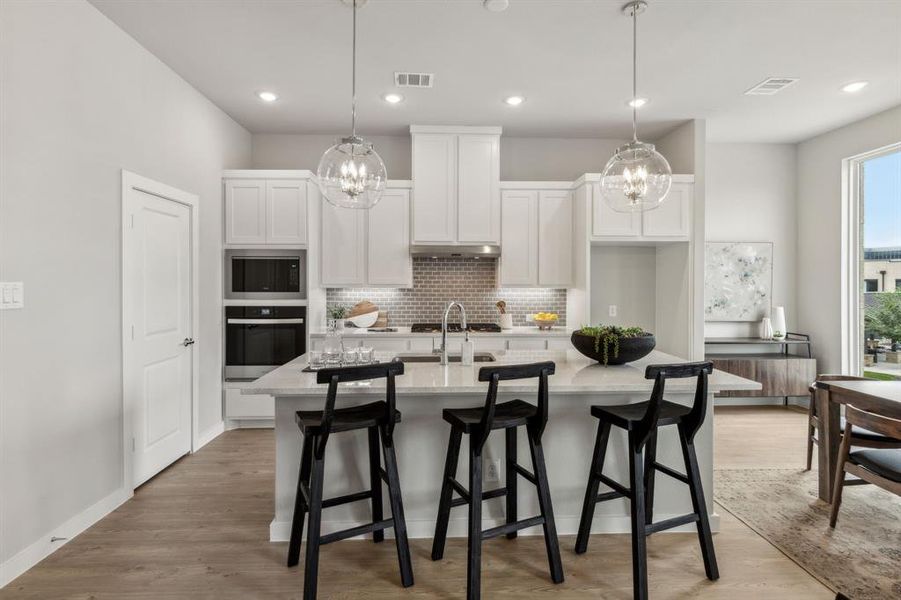 Kitchen featuring tasteful backsplash, a kitchen bar, stainless steel appliances, light hardwood / wood-style floors, and a center island with sink