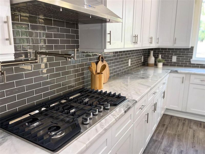 Kitchen with light stone counters, tasteful backsplash, black gas stovetop, dark wood-type flooring, and white cabinets