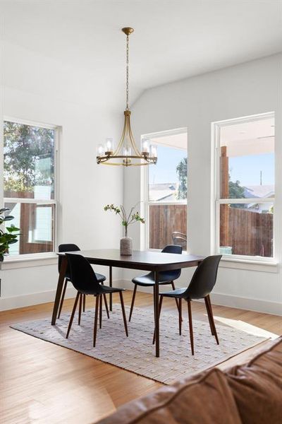 Dining room with a notable chandelier, light hardwood / wood-style floors, lofted ceiling, and a wealth of natural light