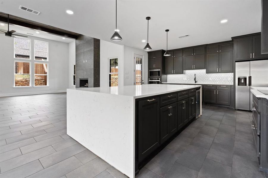 Kitchen with a center island, tile patterned floors, hanging light fixtures, appliances with stainless steel finishes, and a fireplace