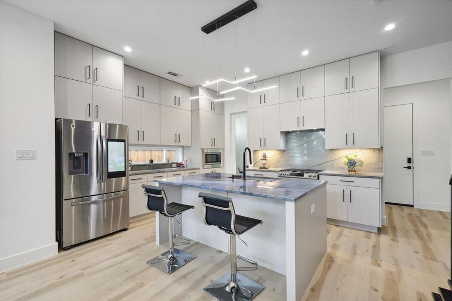 Kitchen featuring decorative light fixtures, stainless steel appliances, light hardwood / wood-style floors, and an island with sink