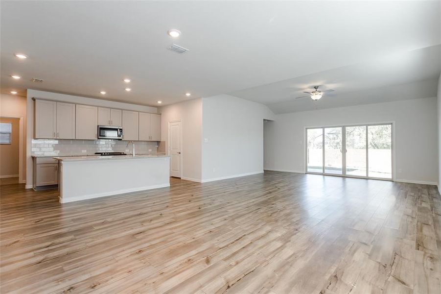 Kitchen with a center island with sink, tasteful backsplash, gray cabinets, ceiling fan, and light wood-type flooring