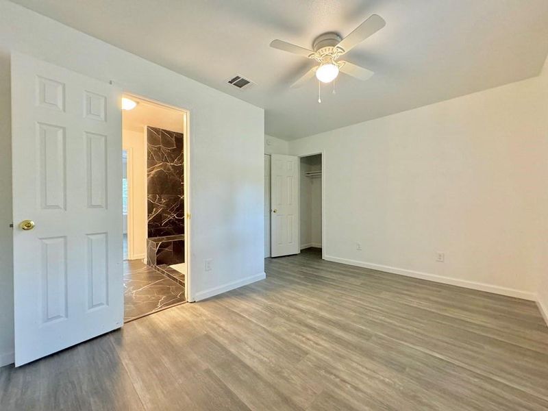 Unfurnished bedroom featuring a walk in closet, a closet, wood-type flooring, and ceiling fan