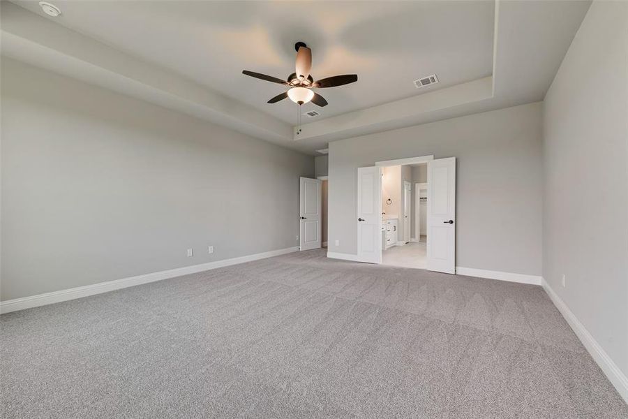 Unfurnished bedroom with a raised ceiling, light carpet, ceiling fan, and ensuite bath