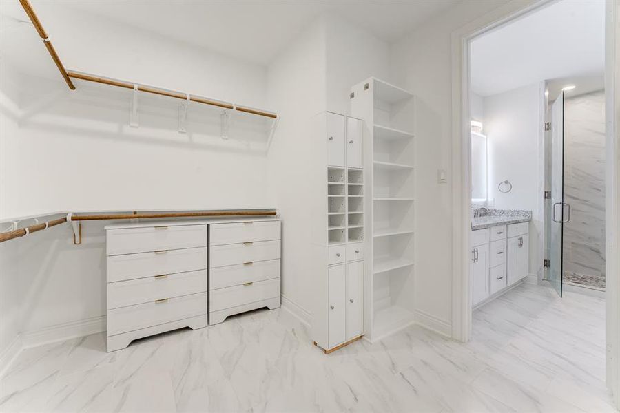 This is a well-organized dream closet with built-in white cabinetry, ample hanging space, and an adjacent modern bathroom.