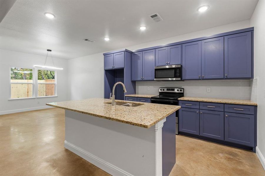 Kitchen featuring hanging light fixtures, light stone counters, an island with sink, appliances with stainless steel finishes, and sink