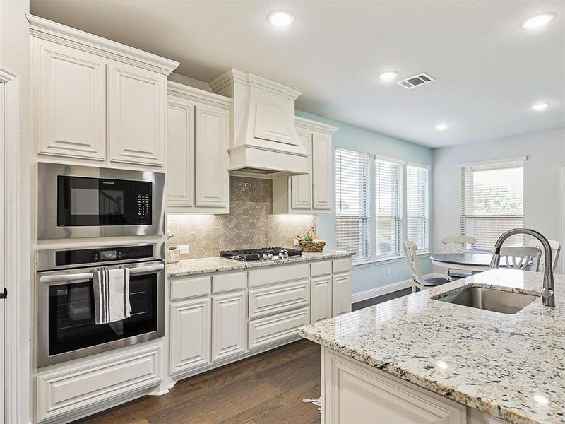 Kitchen featuring dark hardwood / wood-style flooring, appliances with stainless steel finishes, light stone countertops, custom range hood, and sink