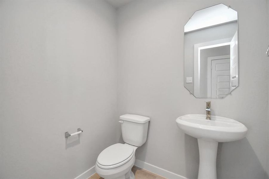 This charming half bathroom, boasting a sophisticated 5-panel door, upgraded pedestal sink, contemporary hardware, and bright recessed lights. Sample photo of completed home with similar floor plan. Actual colors and selections may vary.