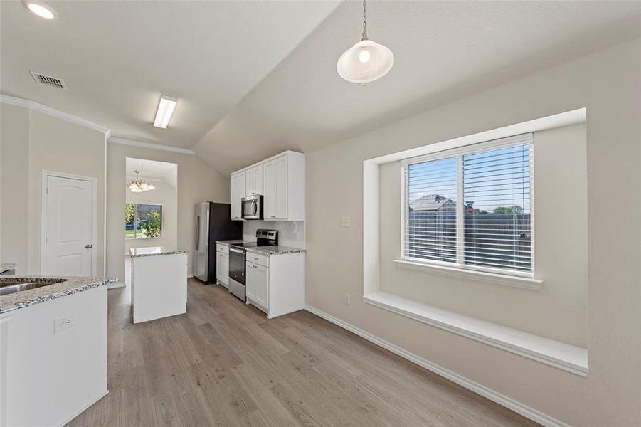 Kitchen with a healthy amount of sunlight, lofted ceiling, stainless steel appliances, and white cabinets