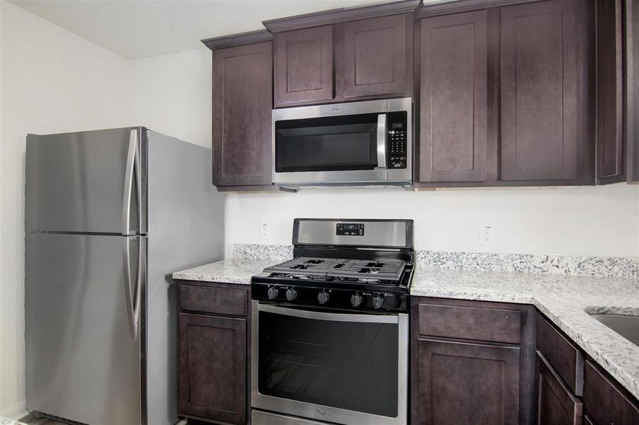 Kitchen featuring appliances with stainless steel finishes, light stone countertops, and dark brown cabinetry