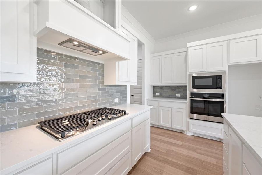 Kitchen featuring light hardwood / wood-style flooring, stainless steel appliances, decorative backsplash, light stone countertops, and white cabinetry