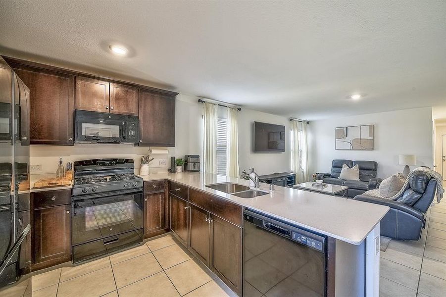 Kitchen with black appliances, light tile patterned flooring, kitchen peninsula, and sink