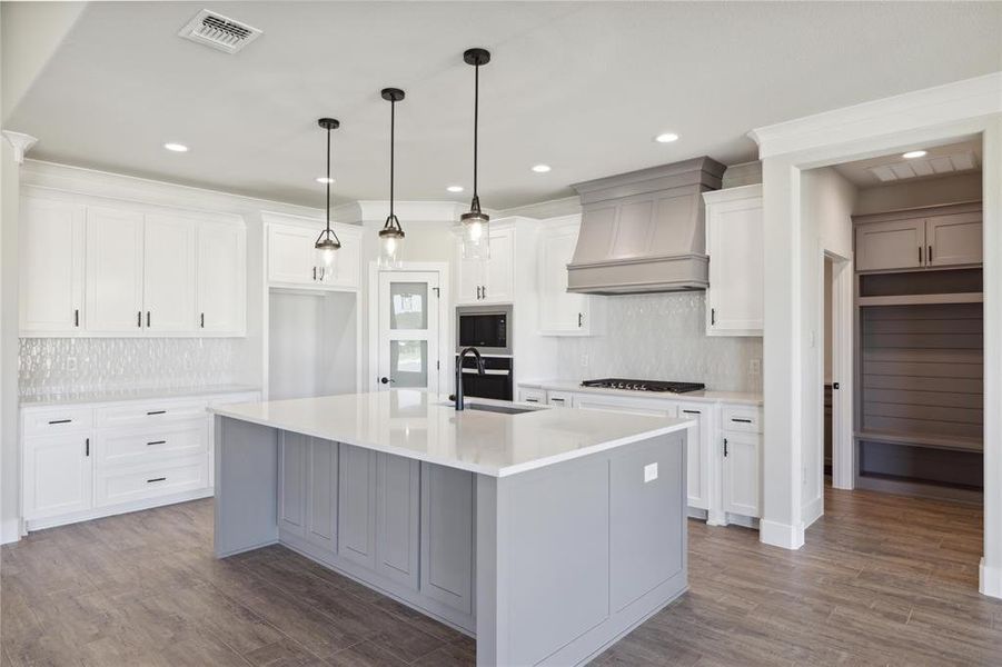 Kitchen featuring custom exhaust hood, a kitchen island with sink, hardwood / wood-style floors, and white cabinetry