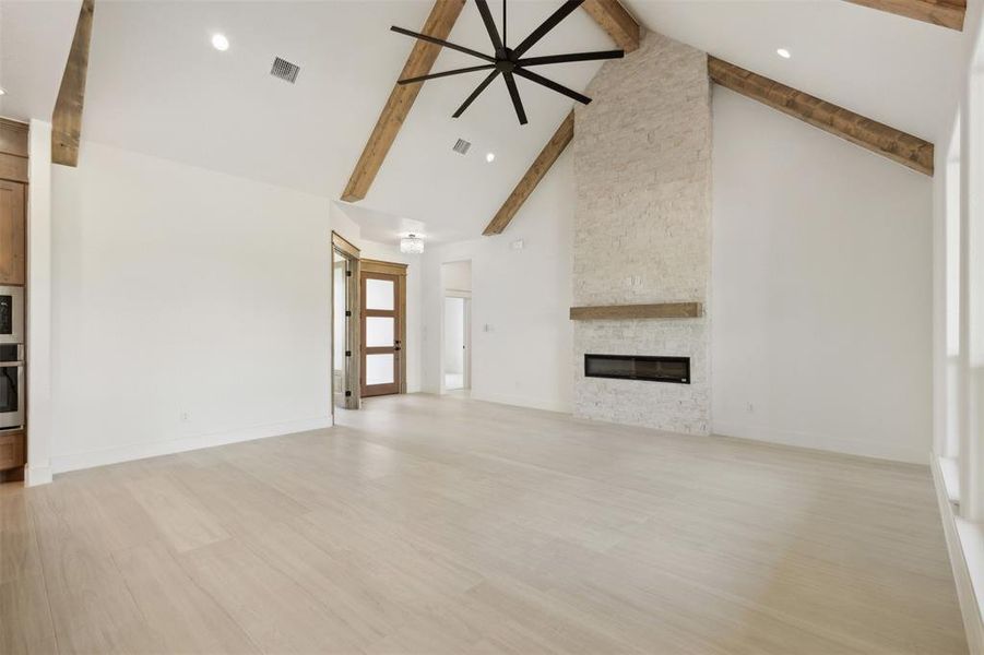 Unfurnished living room featuring a stone fireplace, beamed ceiling, light wood-type flooring, and high vaulted ceiling