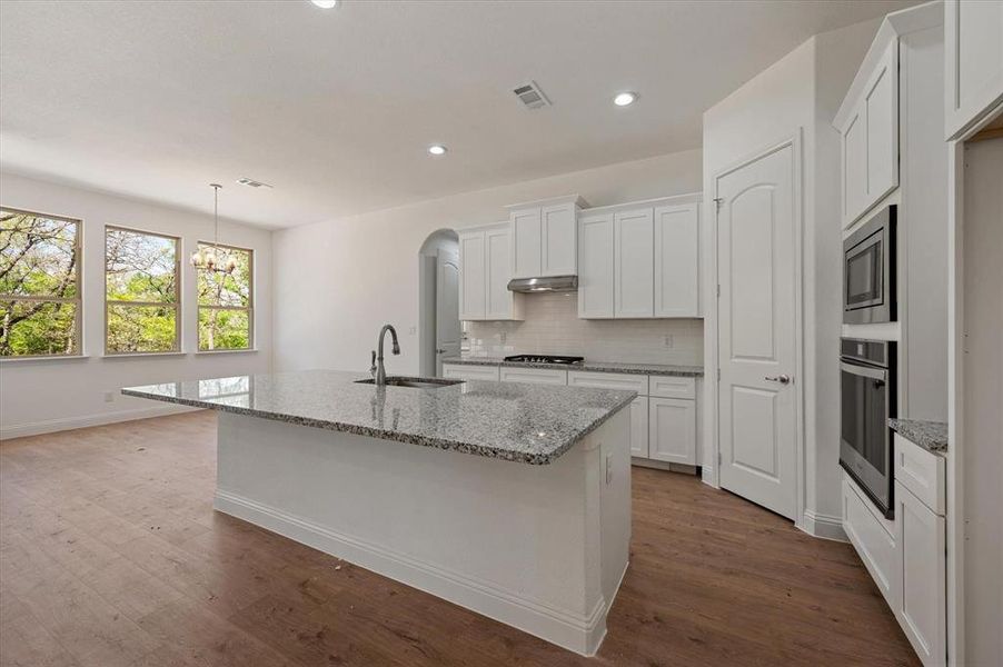 Kitchen with a center island with sink, sink, stainless steel appliances, and wood-type flooring