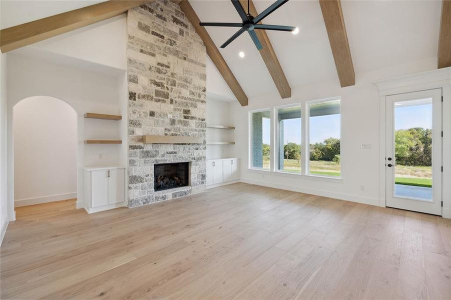 Unfurnished living room featuring a stone fireplace, high vaulted ceiling, ceiling fan, beam ceiling, and light wood-type flooring