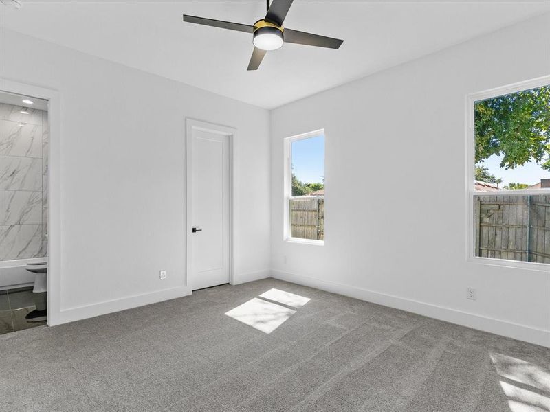 Unfurnished bedroom with ensuite bath, ceiling fan, and light colored carpet