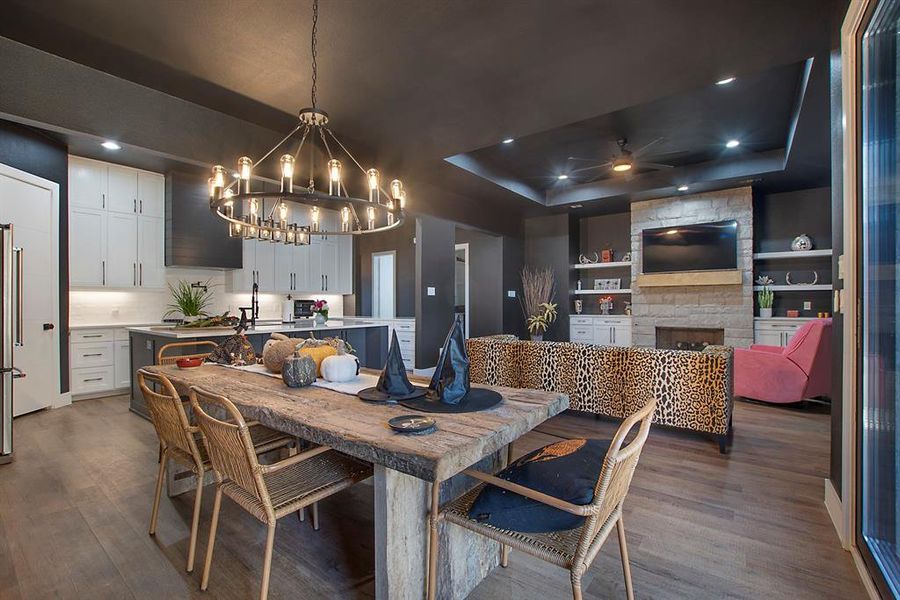 Dining area featuring a stone fireplace, a tray ceiling, wood-type flooring, built in shelves, and ceiling fan with notable chandelier